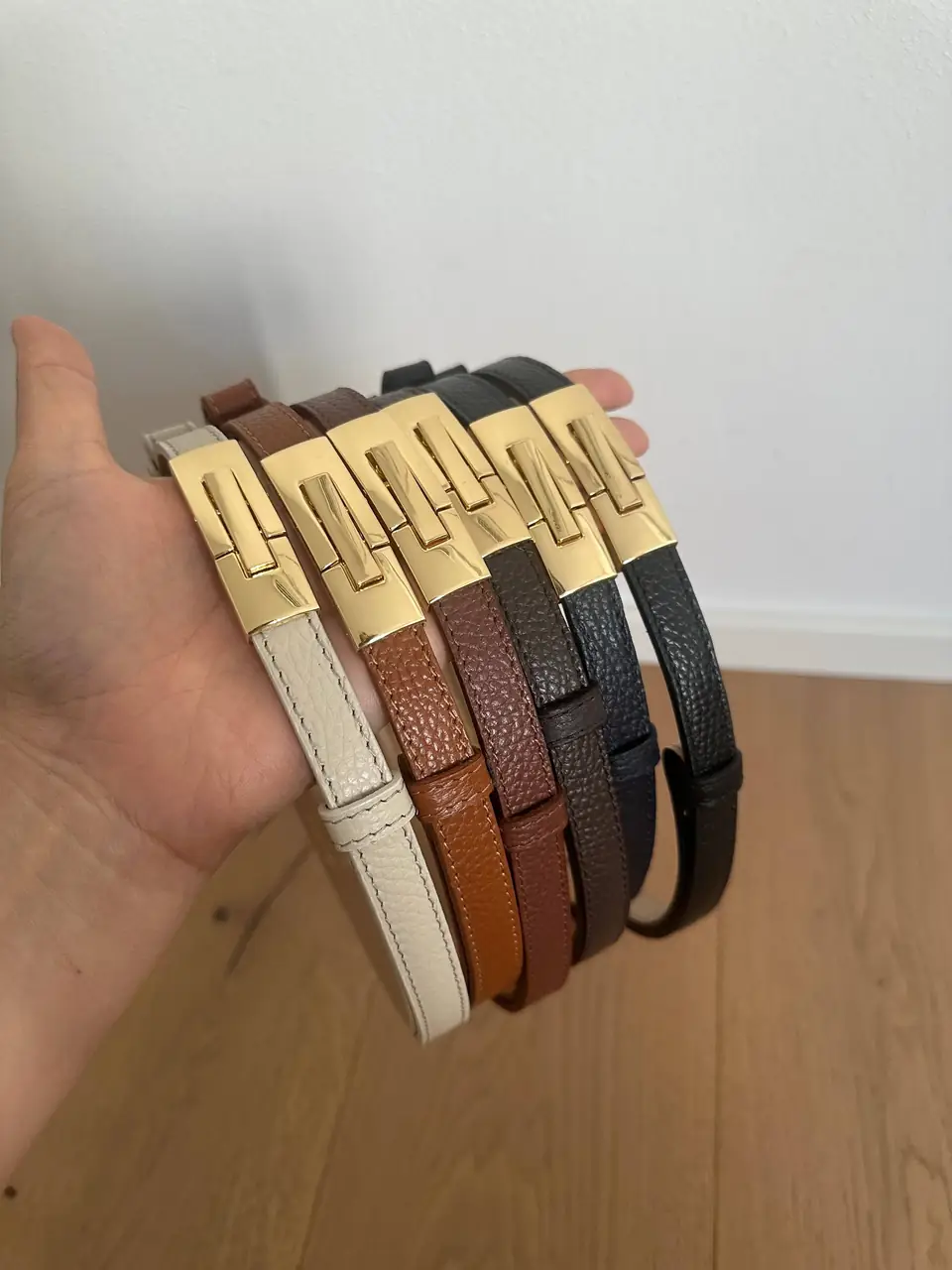 Five Italian leather skinny belts with gold buckles held in one hand