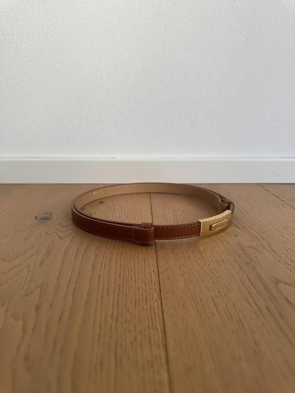 The cognac skinny belt buckled on a wood floor