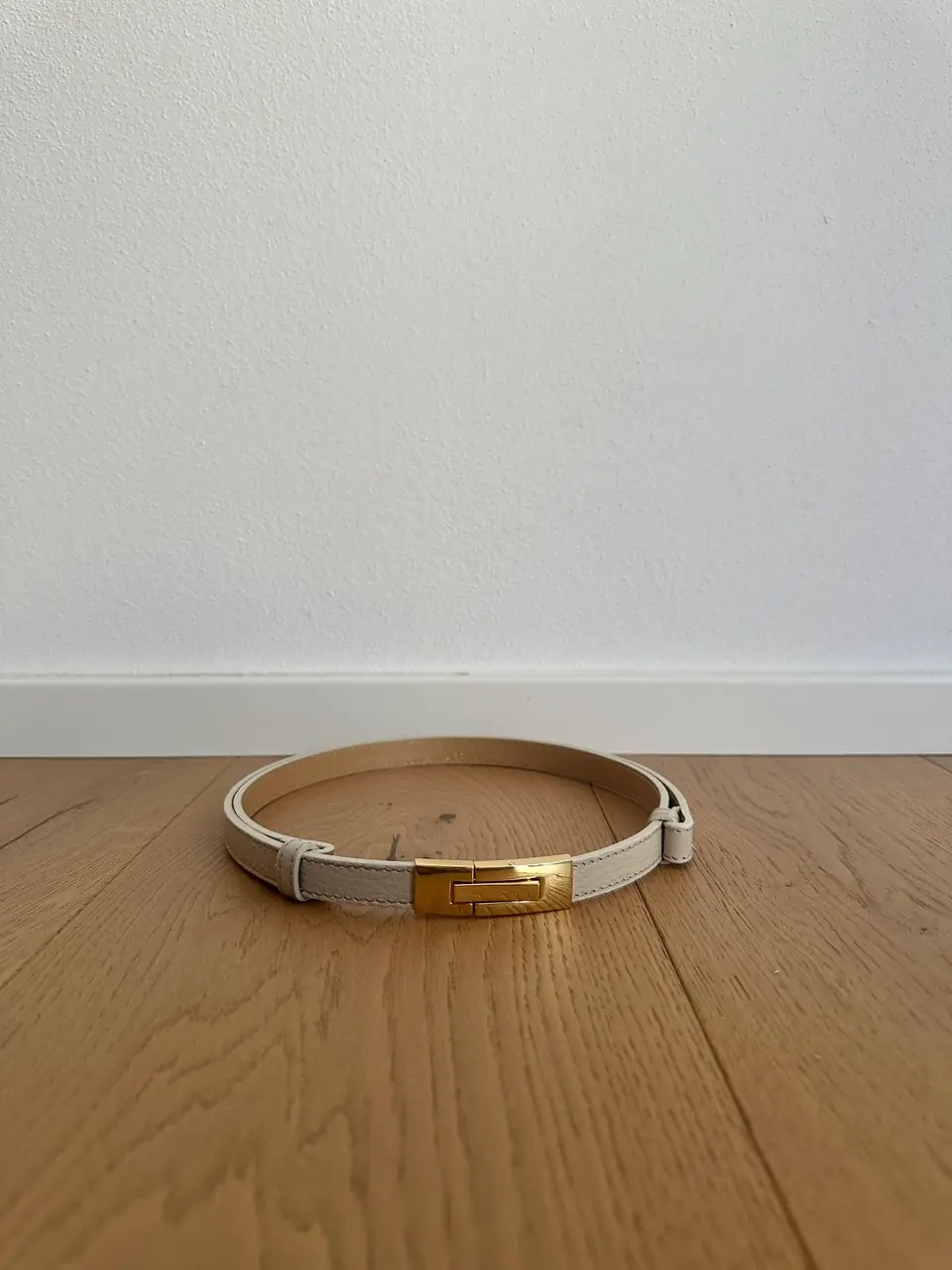 The cream skinny belt buckled on a wood floor