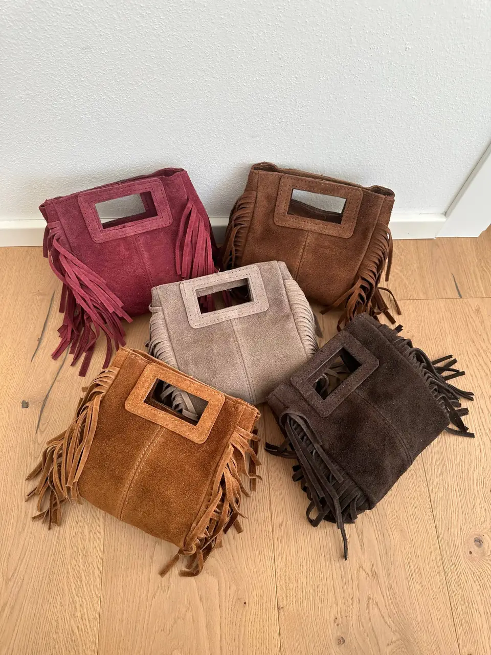 Italian suede mini fringe bags in five colours on a wood floor