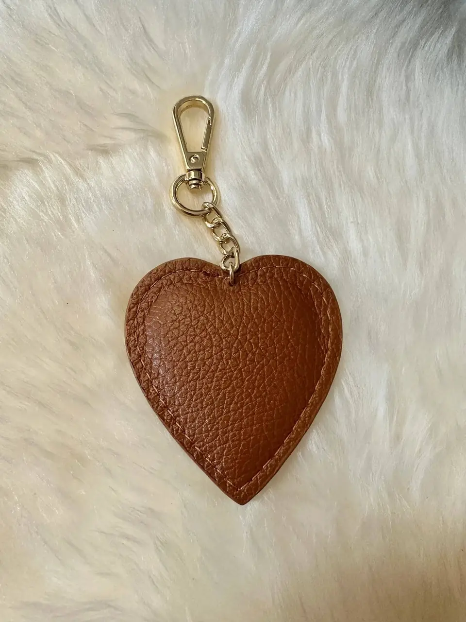 A cognac leather heart charm with a gold clasp